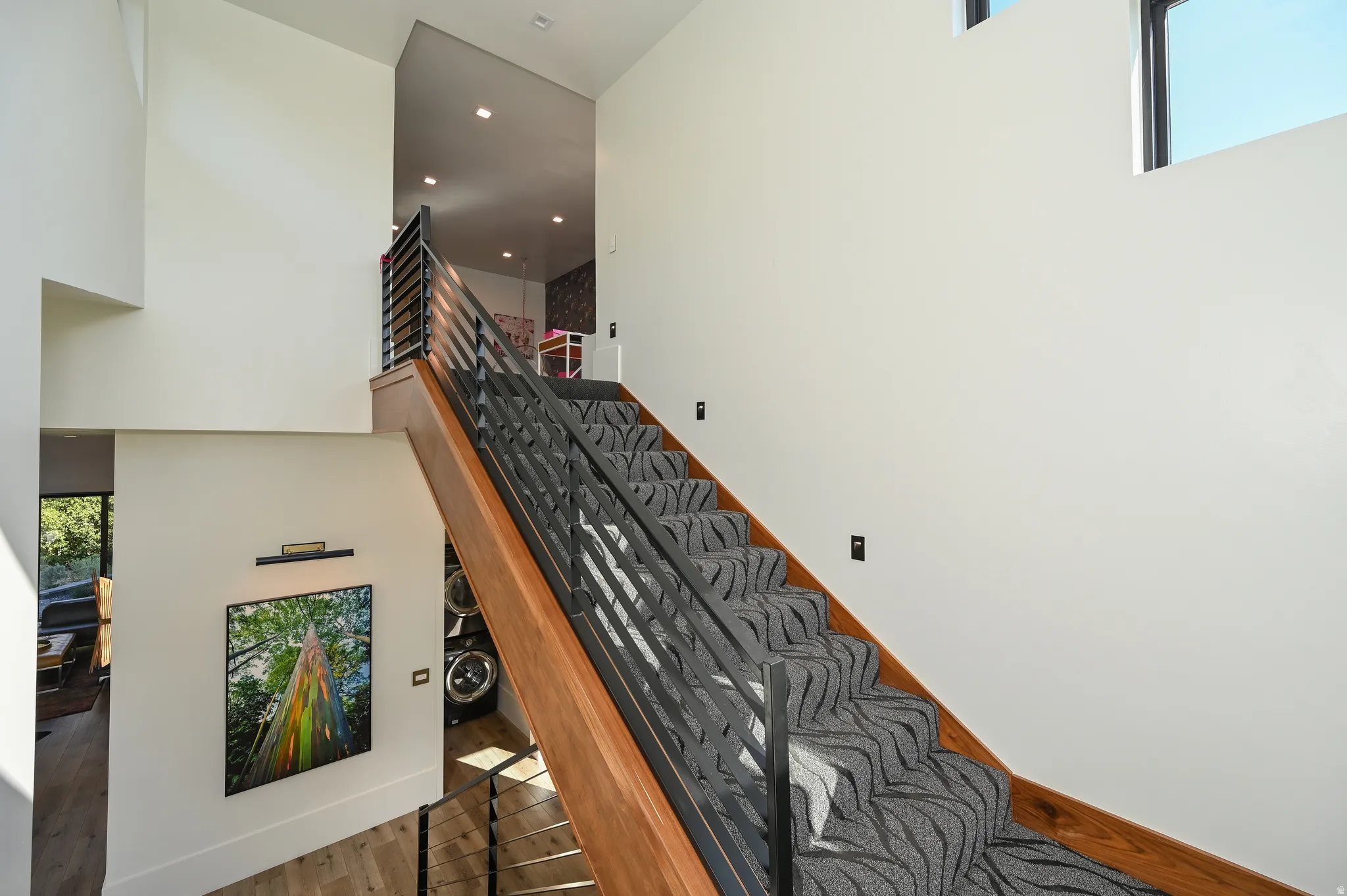 Staircase featuring wood-finish handrails, black metal balusters, and patterned carpet treads