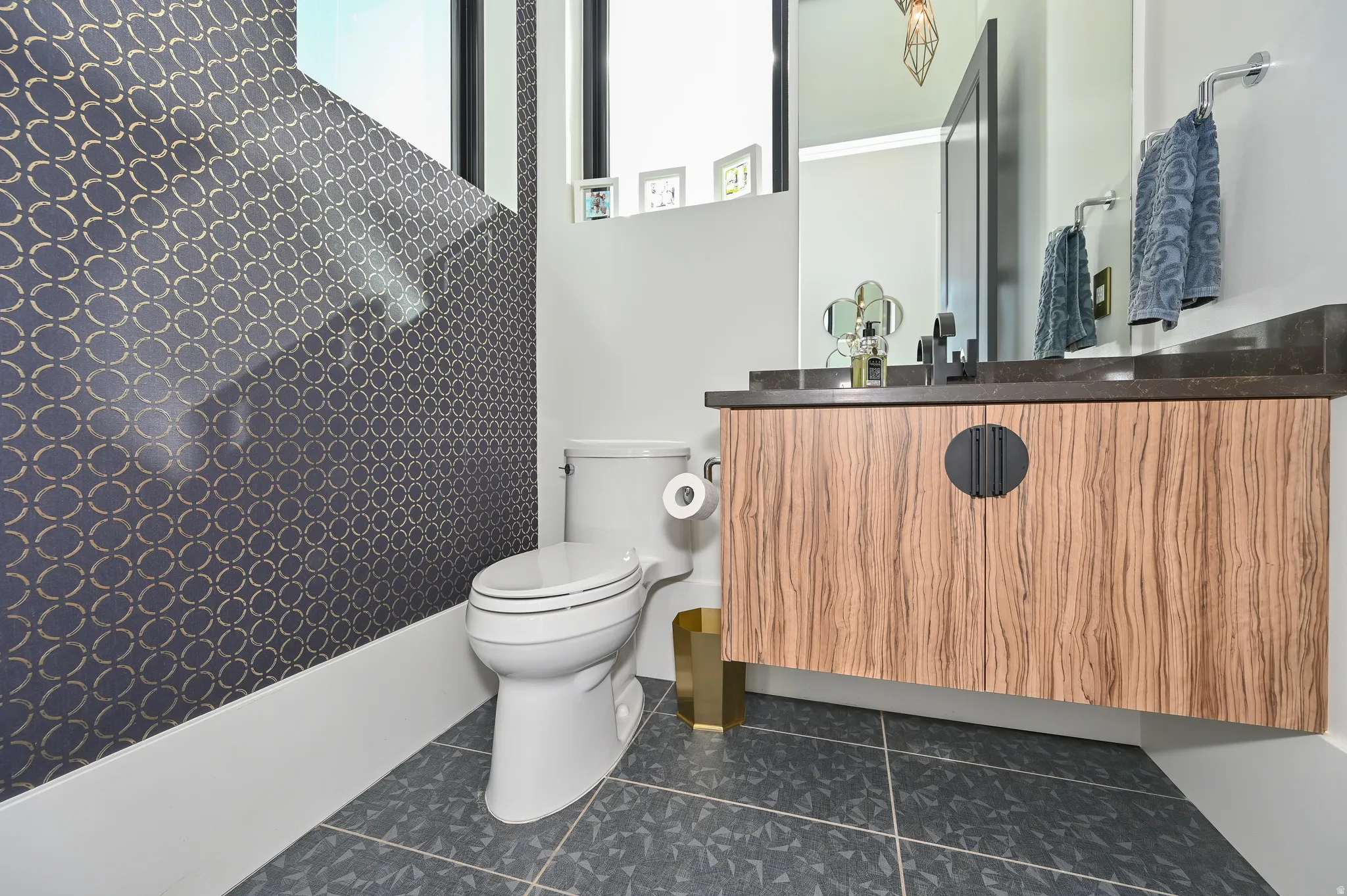 Bathroom featuring a patterned accent wall, a floating wood-finish vanity with a dark countertop, a rectangular mirror, and dark floor tiles