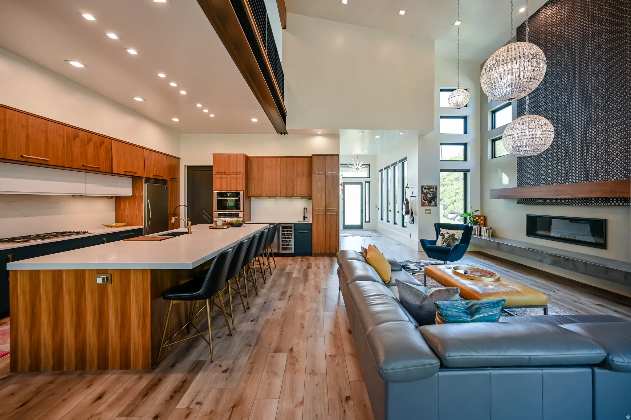 Expansive open-concept living space featuring high ceilings, wood-finish flooring, a contemporary linear fireplace, and a kitchen island with seating