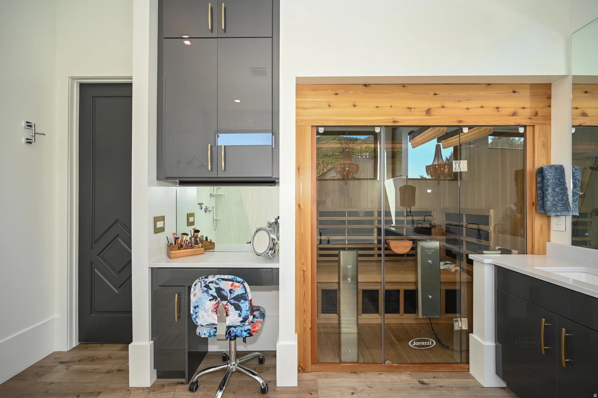 Spa-like bathroom with a glass-enclosed sauna featuring wood paneling, a dedicated vanity area with gray cabinetry and stone countertop, and wood-finish flooring