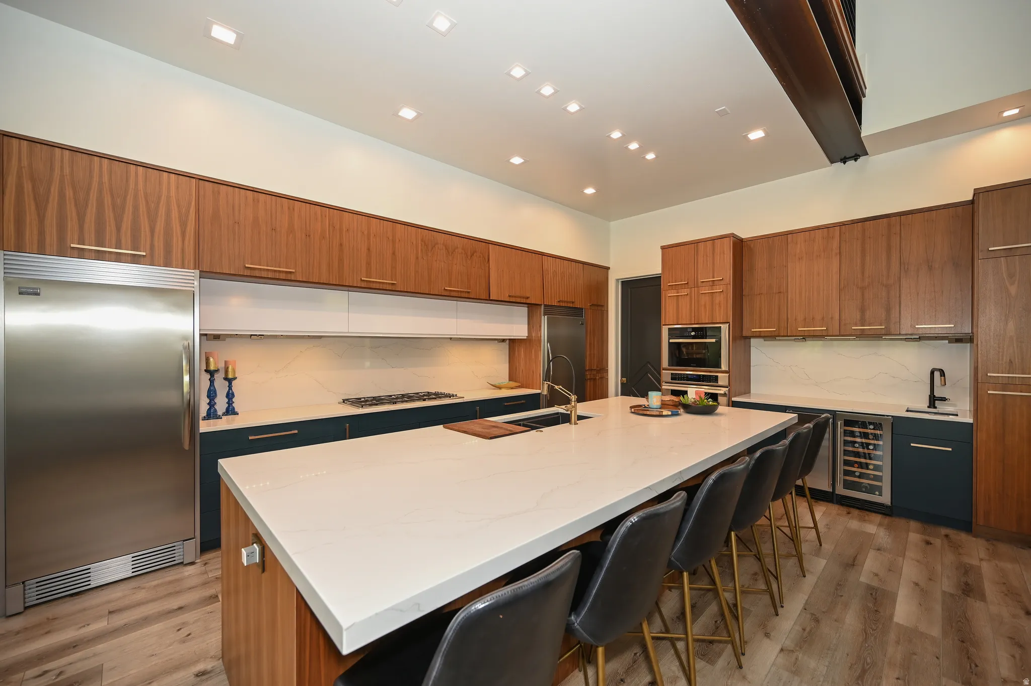 Gourmet kitchen featuring a large central island with seating, stainless steel appliances, extensive wood-finish cabinetry, a built-in wine refrigerator, and wood-finish flooring