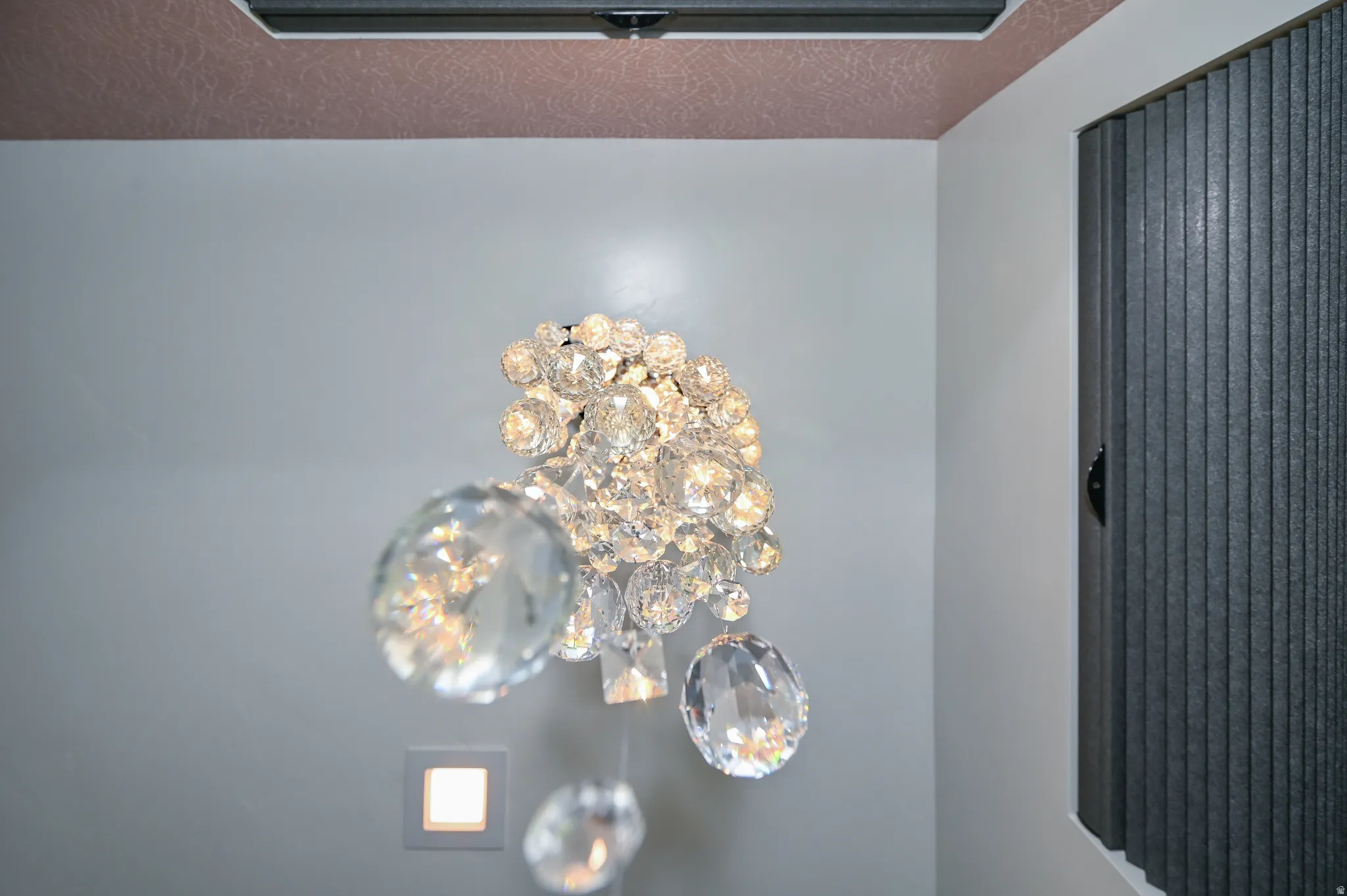 Crystal chandelier lighting with a square recessed light fixture, textured ceiling detail, and vertical blinds