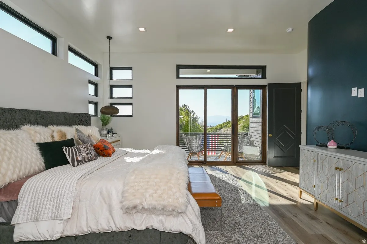 Bedroom featuring a private balcony with glass sliding doors, multiple transom windows, and wood-finish flooring