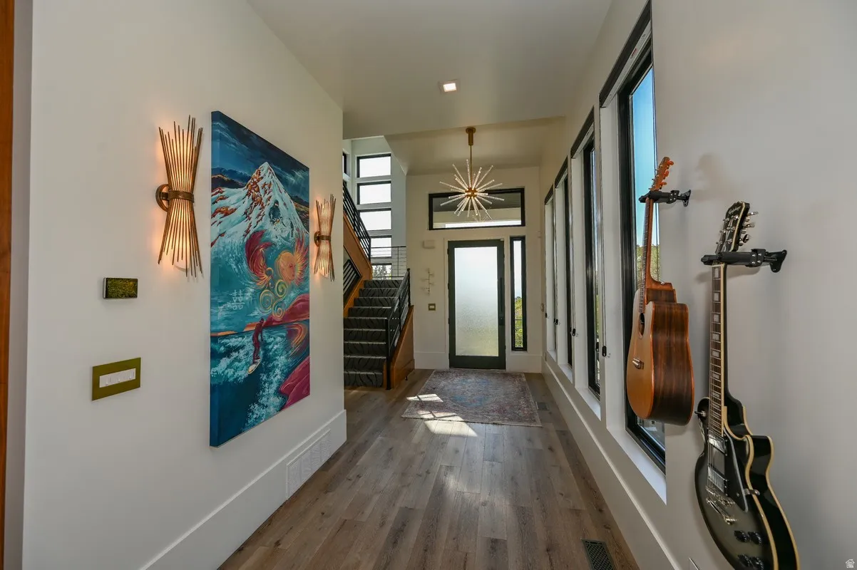 Entryway featuring wood-finish flooring, a contemporary chandelier, multiple windows with dark trim, a staircase with dark risers and light treads, and a frosted glass door with a transom window
