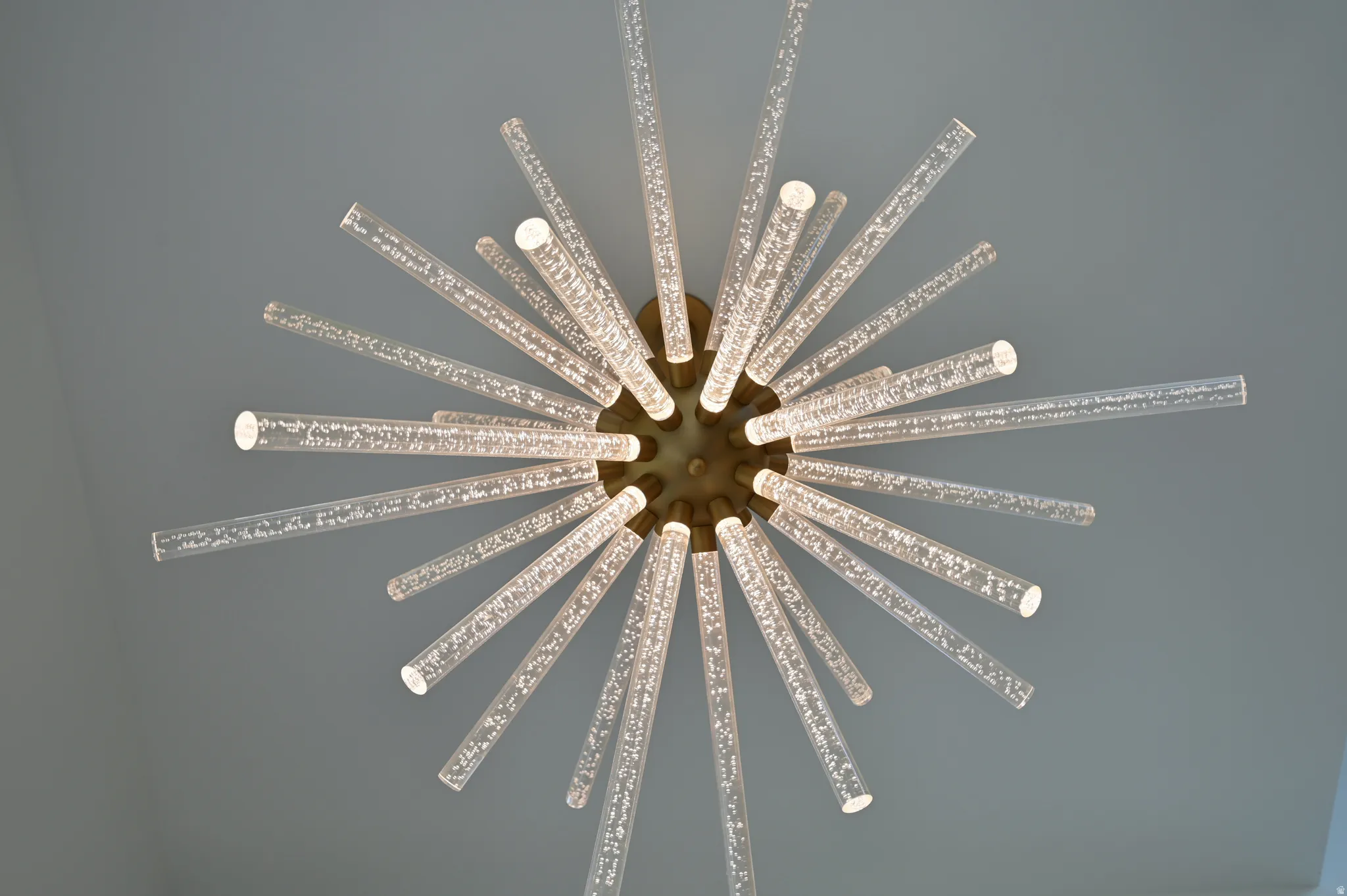 Contemporary ceiling light fixture featuring numerous clear acrylic rods with internal bubble detailing, radiating from a central bronze-finish base, providing ambient illumination