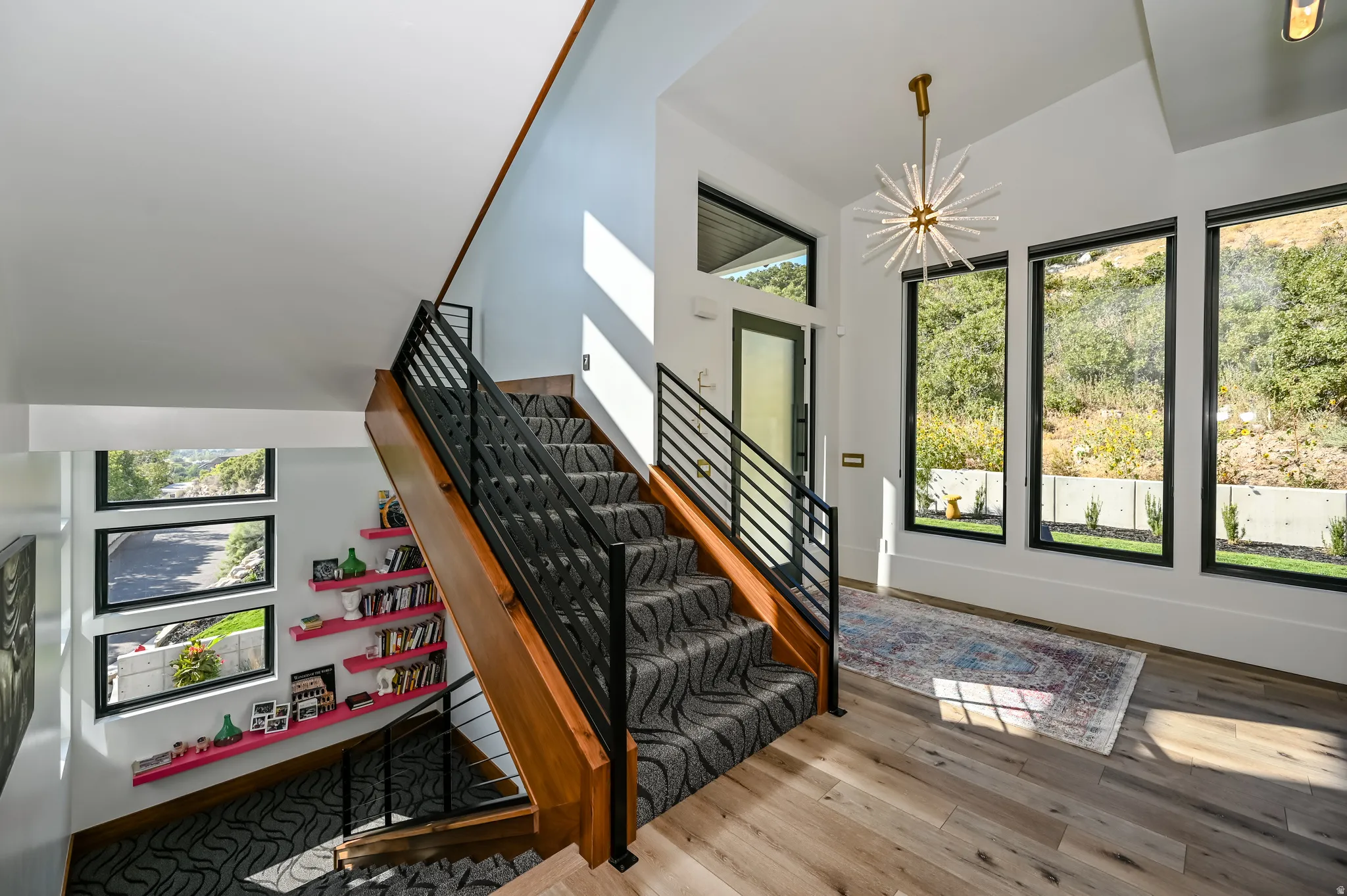 Entry foyer featuring light wood-finish flooring, a contemporary chandelier, and three tall windows with black frames