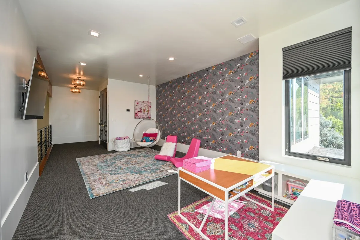 Carpeted room featuring a patterned accent wall, a built-in window seat with integrated storage, and a large window with a roller blind
