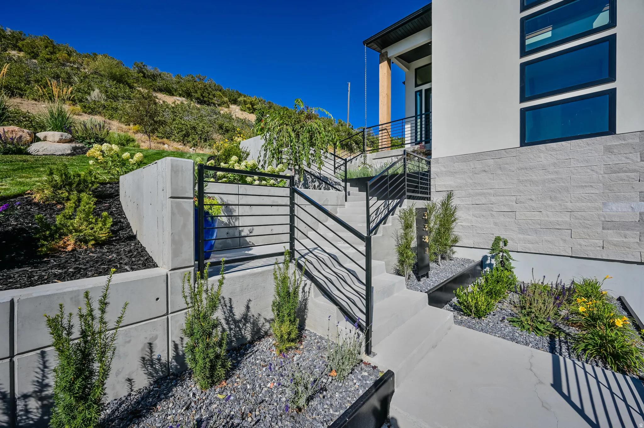 Front exterior featuring concrete steps with black metal railings, a white stucco facade, and a stone accent wall