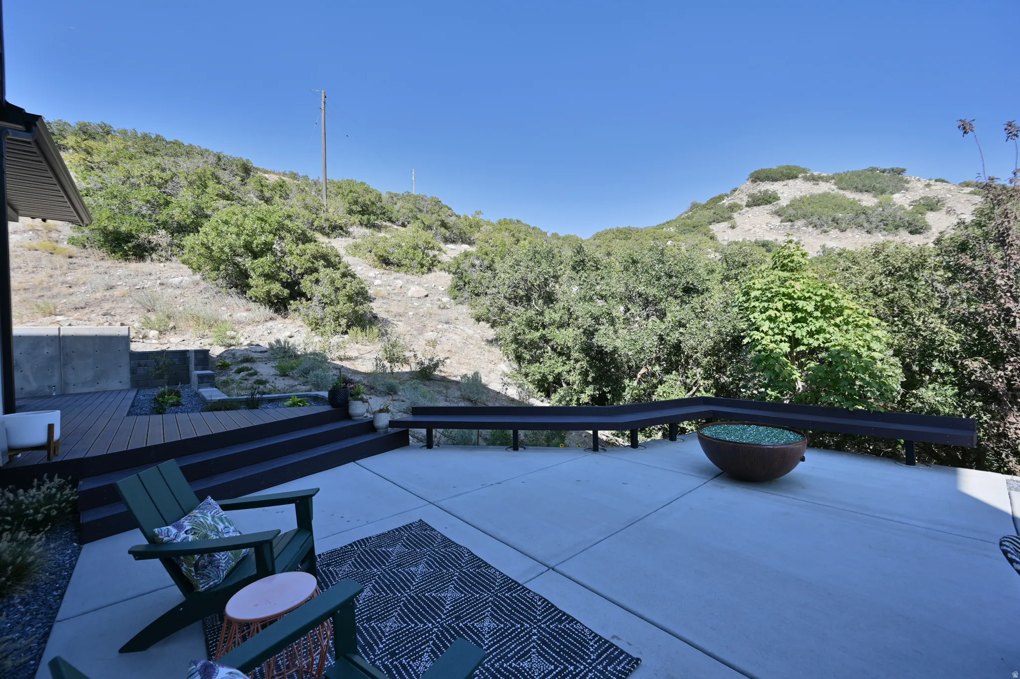 Expansive concrete patio with a tiered composite deck, built-in bench seating, and a decorative fire pit