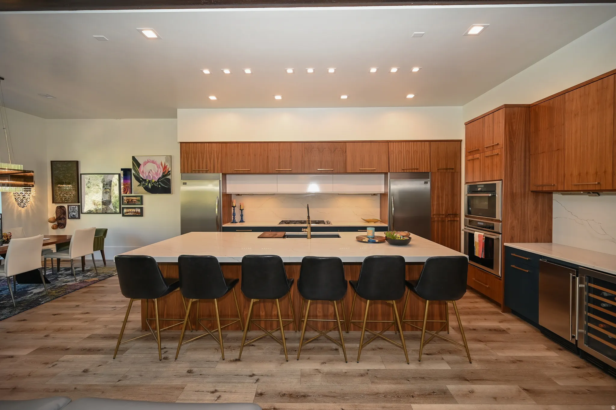Spacious kitchen featuring a large central island with seating, wood-finish flooring, full-height wood cabinetry, stainless steel appliances, and integrated wine refrigeration
