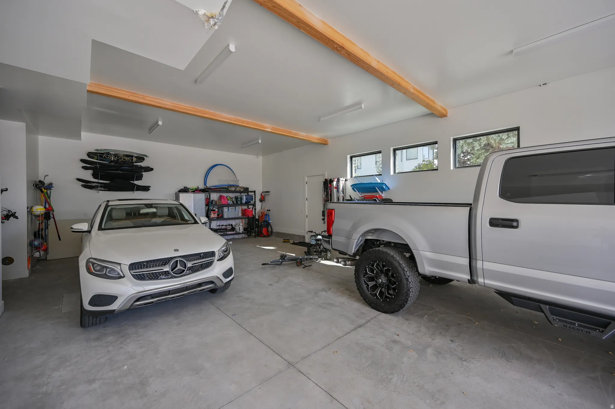 Spacious garage featuring a concrete floor, exposed wood ceiling beams, overhead fluorescent lighting, and multiple windows
