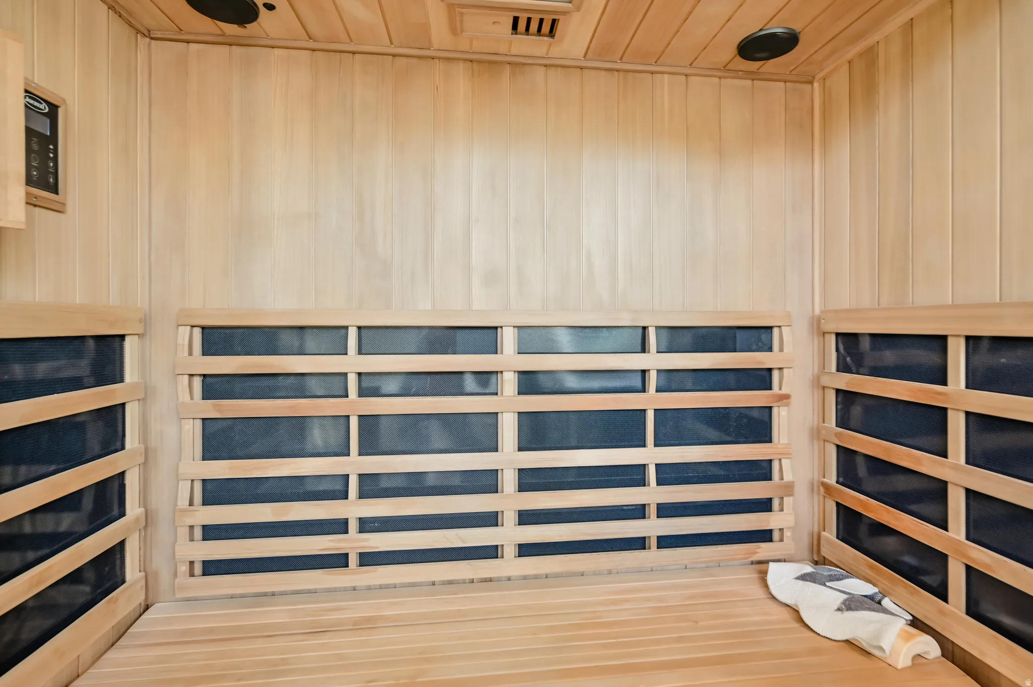 Custom sauna featuring light-toned wood paneling throughout, built-in wooden bench seating, and wall-mounted control panel