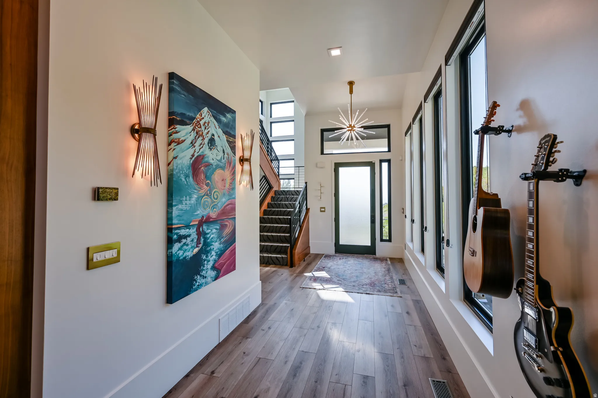 Foyer featuring wood-finish flooring, a contemporary chandelier, multiple windows with dark trim, a staircase with dark treads, and a frosted glass entry door