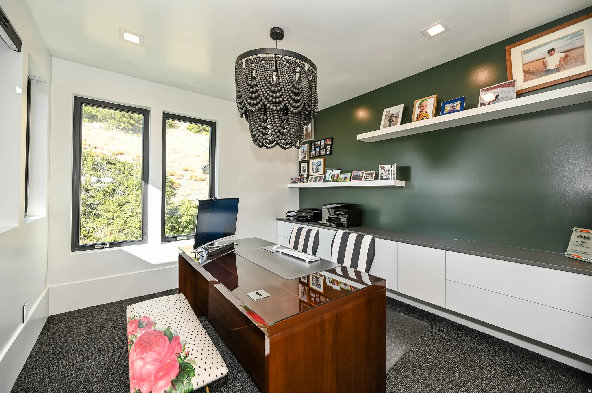 Dedicated space featuring a dark green accent wall with floating shelves, built-in white cabinetry with a contrasting countertop, and a dark, ornate chandelier