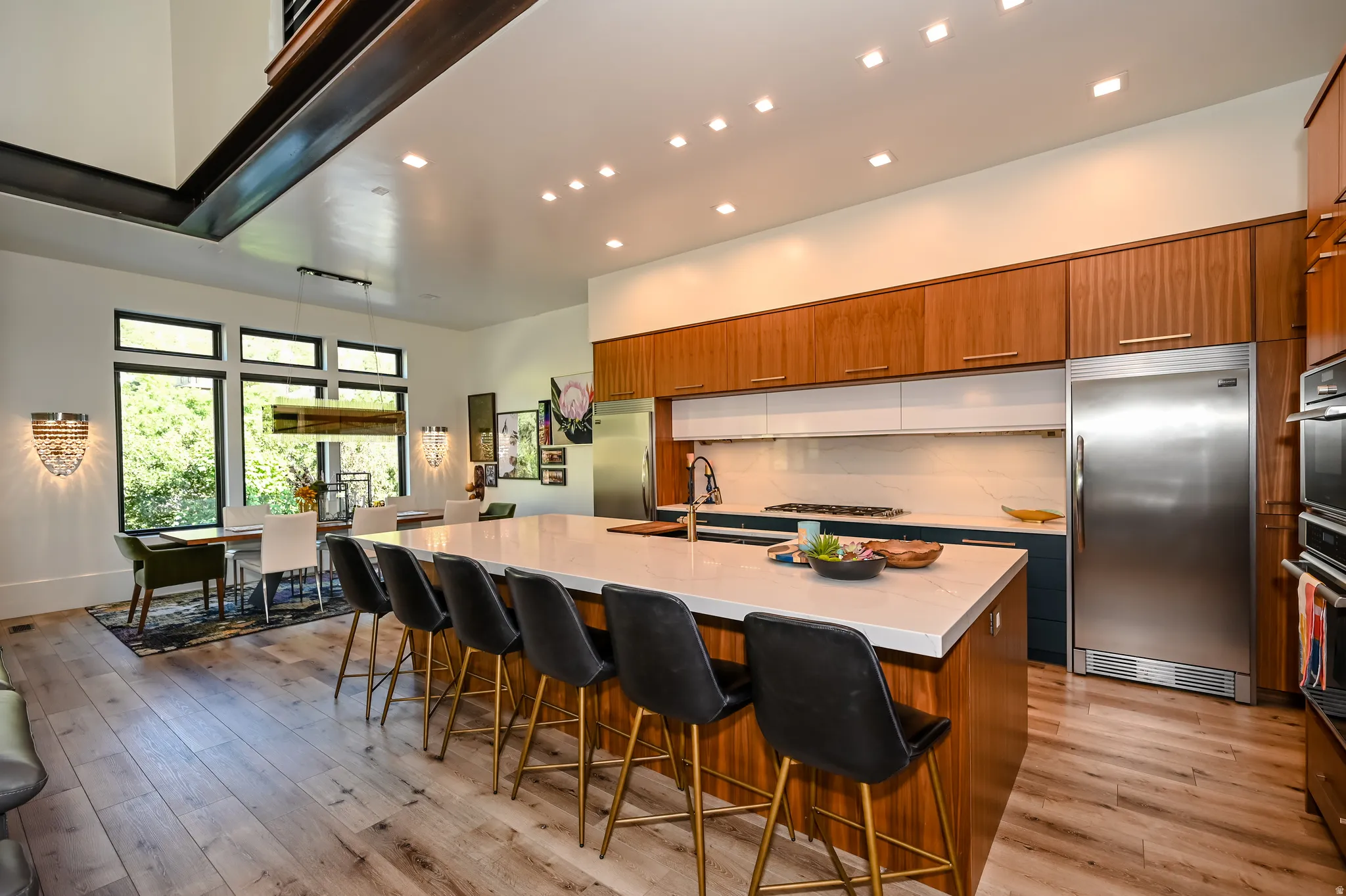 Open-concept kitchen featuring an expansive island with seating, wood-finish flooring, and integrated stainless steel appliances