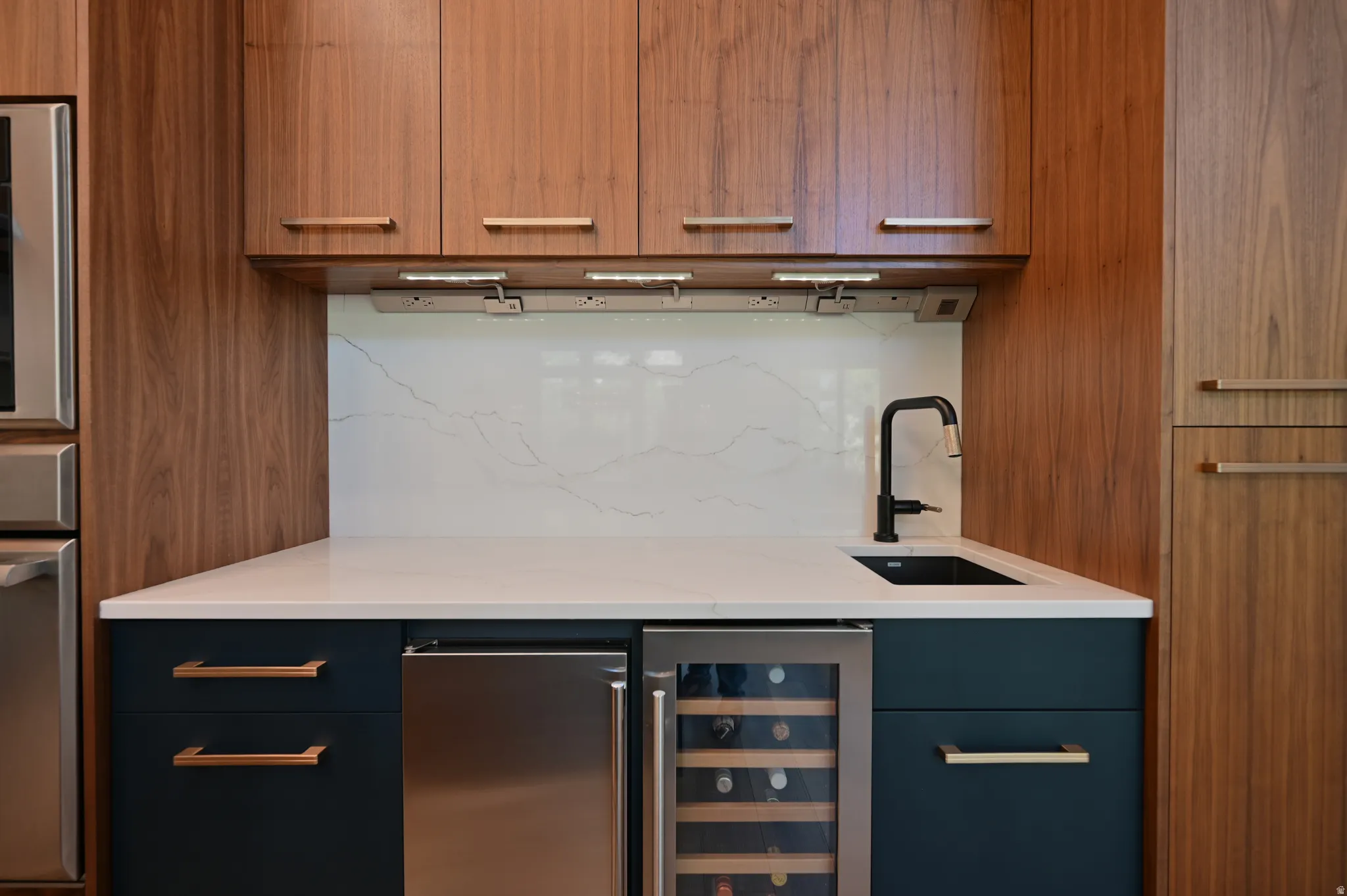 Built-in beverage station featuring wood-finish cabinetry, solid surface countertop, matte black faucet, and under-counter wine refrigerator