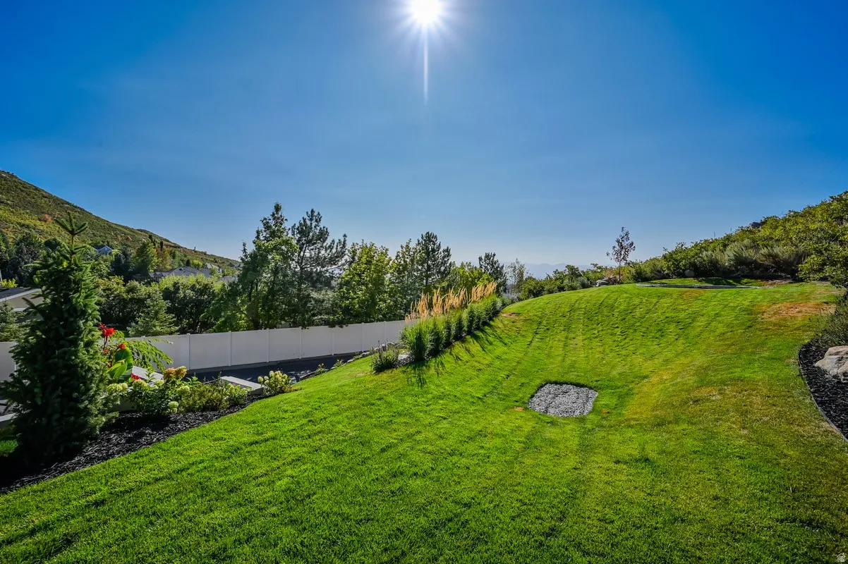 Expansive green lawn with mountain backdrop, bordered by mature trees and shrubs