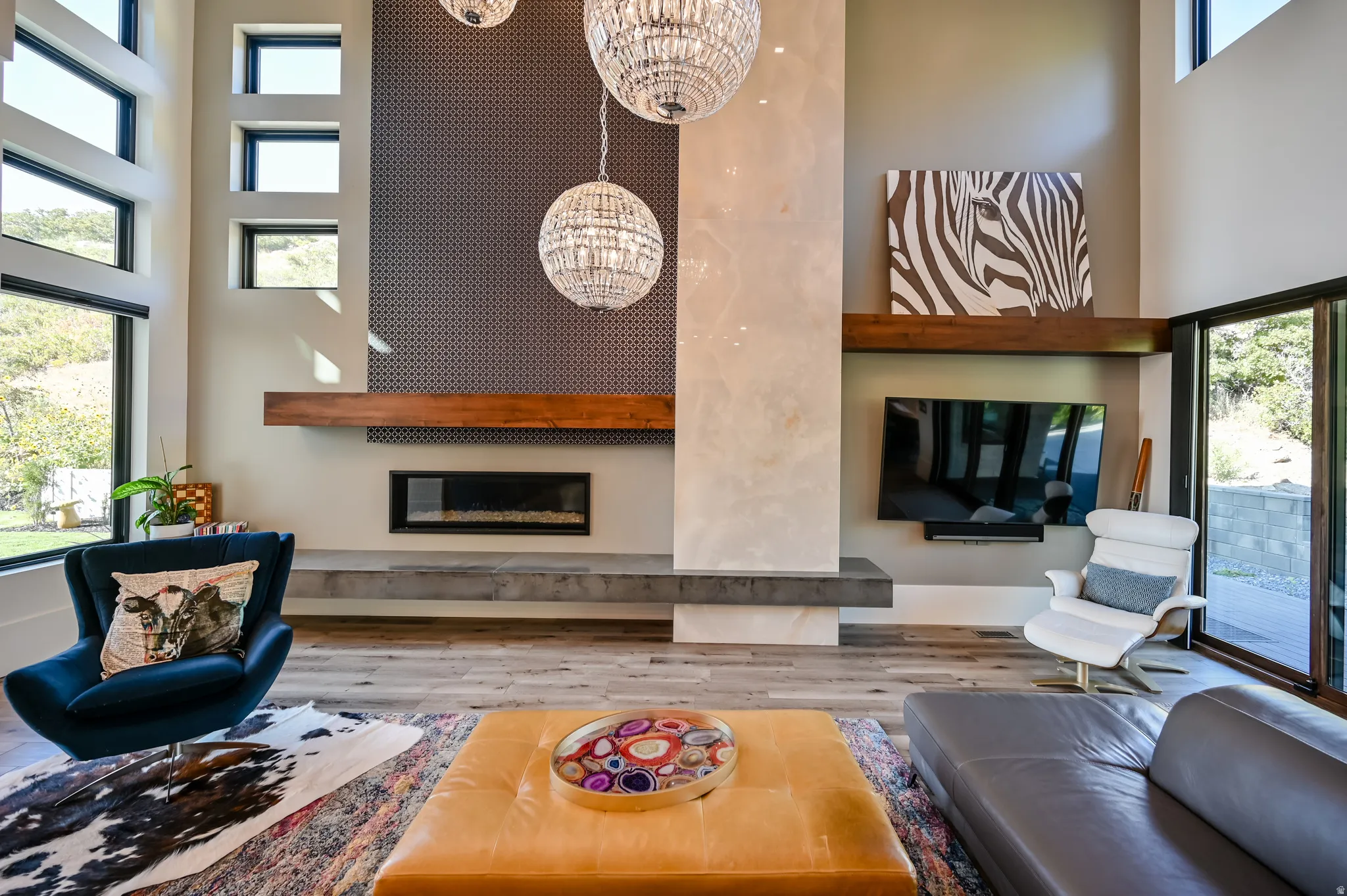 Great room featuring a linear fireplace with a concrete-finish hearth, a wood mantel, a textured accent wall, and multiple floor-to-ceiling windows