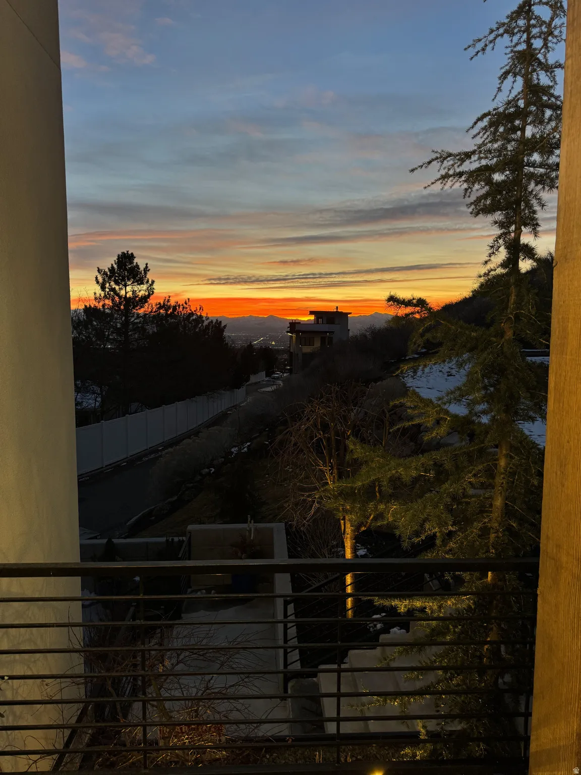 Elevated outdoor balcony with horizontal metal railings, overlooking a distant horizon with a vibrant sky
