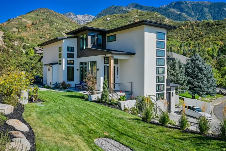 Contemporary architecture featuring a white stucco facade, dark trim accents, extensive window placements, a manicured lawn, and natural rock landscaping elements