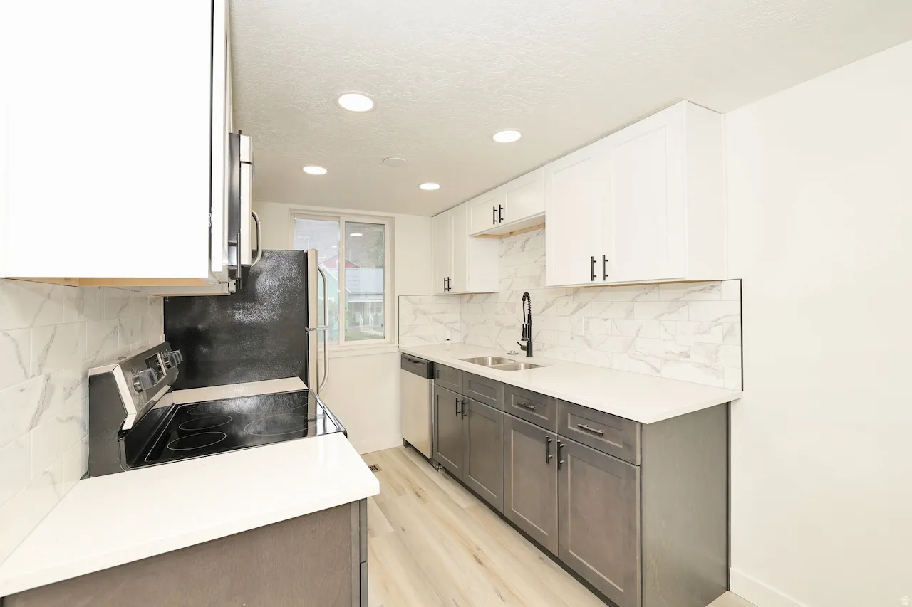 Modern kitchen featuring white upper cabinetry, gray lower cabinetry, light wood-finish flooring, white countertops, and a marble-patterned tile backsplash