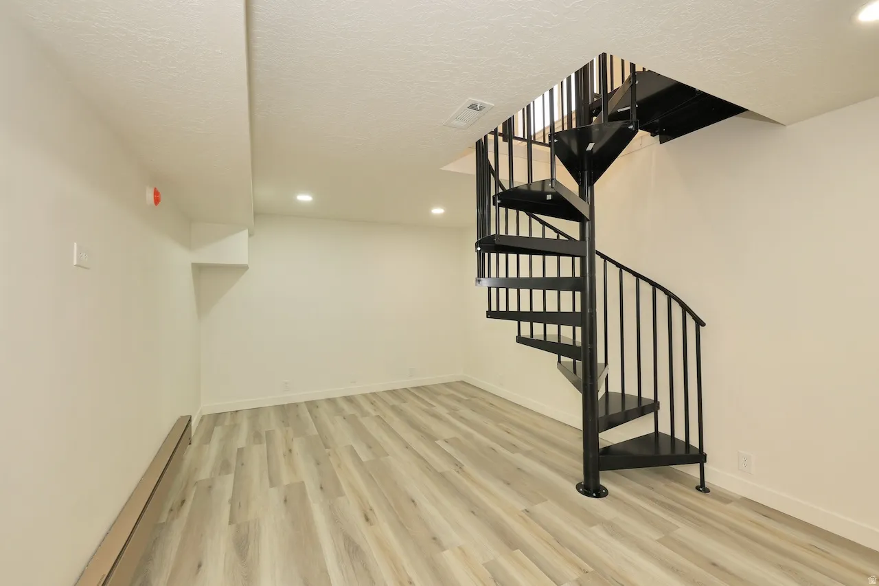 Expansive room featuring a black spiral staircase with metal balusters, wood-finish flooring, recessed lighting, and crisp white walls