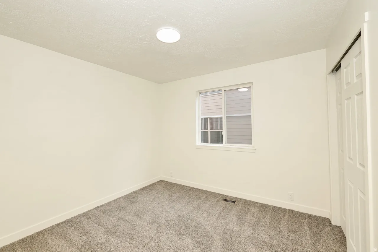 Bright interior space featuring a window with blinds, neutral wall paint, and gray carpet flooring