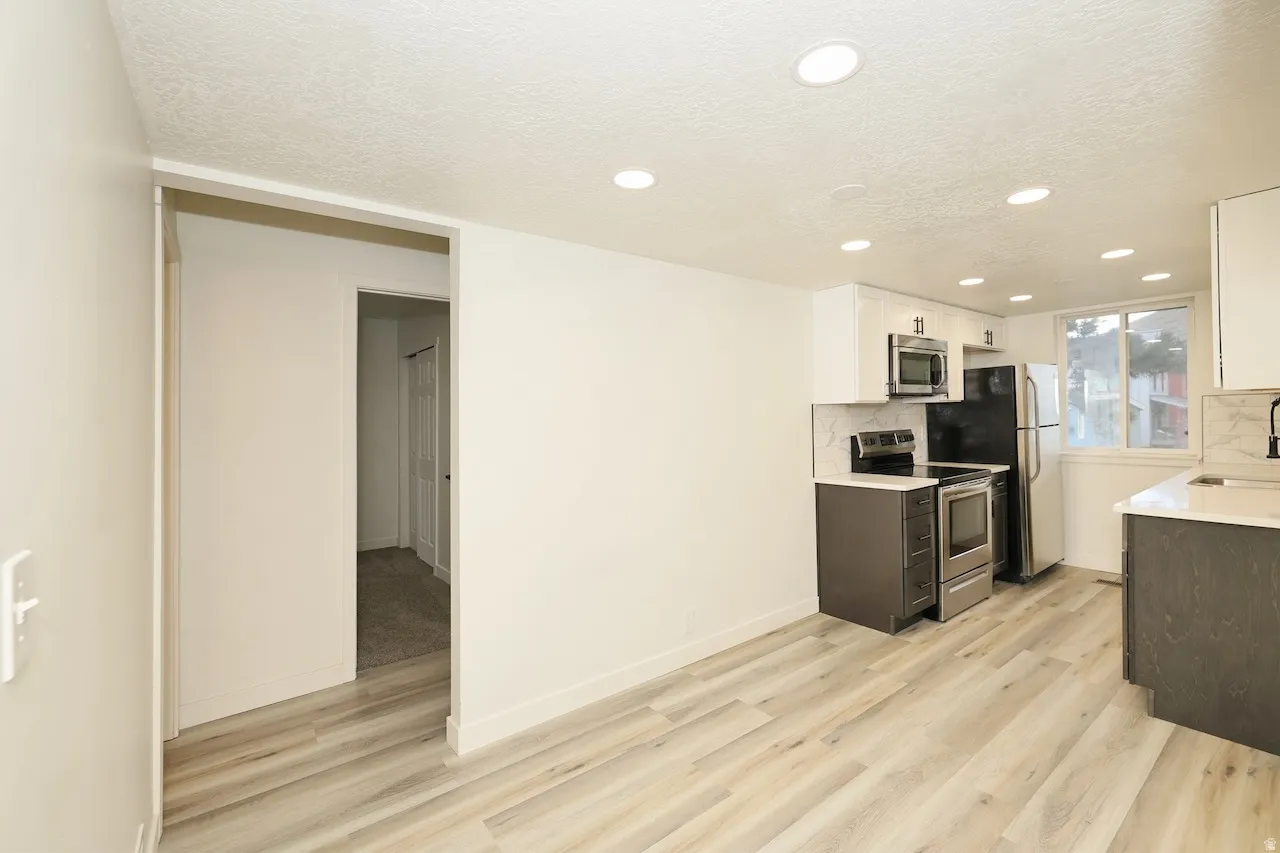 Contemporary kitchen featuring stainless steel appliances, light wood-finish flooring, recessed lighting, white upper cabinetry, and dark lower cabinetry