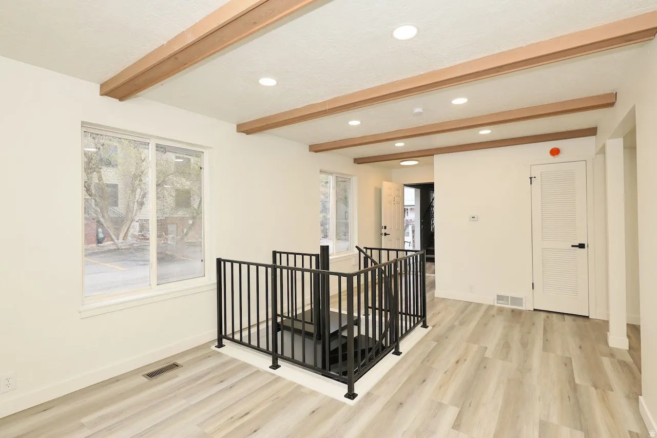 Expansive open-concept room featuring wood-finish flooring, exposed wood ceiling beams, and recessed lighting