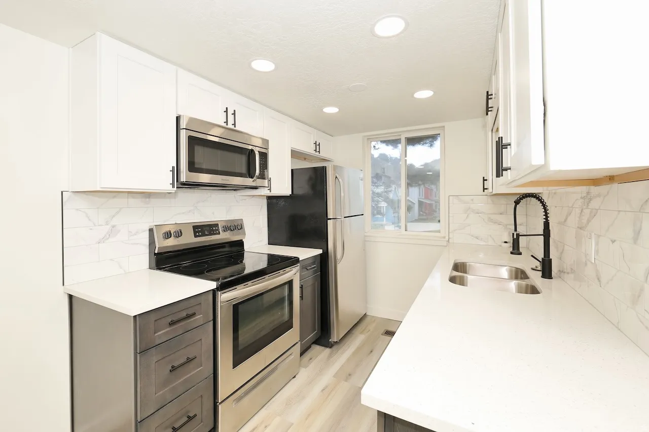 Contemporary kitchen featuring white shaker upper cabinetry and gray lower cabinetry, stainless steel appliances, a white solid surface countertop, and a white marble-look subway tile backsplash