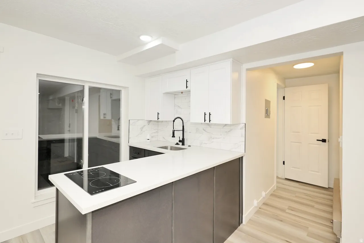 Modern kitchen featuring white shaker cabinetry, an integrated cooktop on the island, quartz countertops, and a white subway tile backsplash