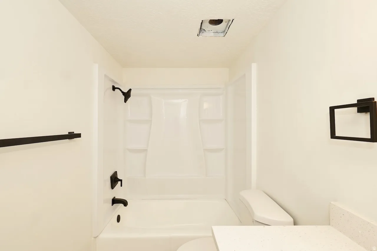 Bathroom with white fiberglass tub and shower surround, matte black fixtures, white walls, and a white countertop