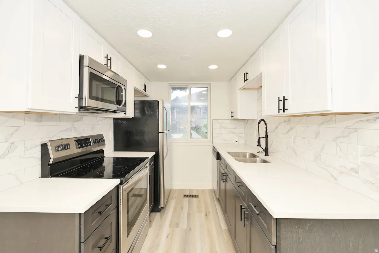 Contemporary kitchen featuring white upper cabinetry, dark lower cabinetry, light countertops, a white subway tile backsplash, and stainless steel appliances