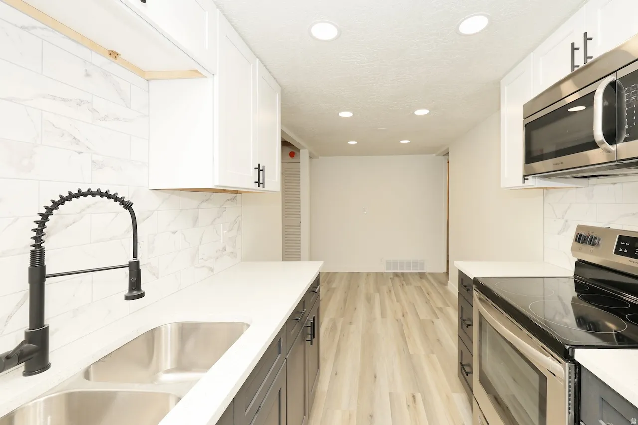 Modern kitchen featuring white upper cabinetry, dark lower cabinetry, light countertops, a double stainless steel sink with a matte black faucet, and a subway tile backsplash