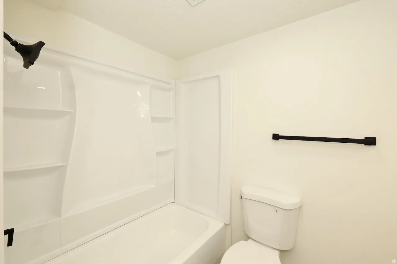 White bathtub and shower combination unit featuring an integrated shower head and shelving