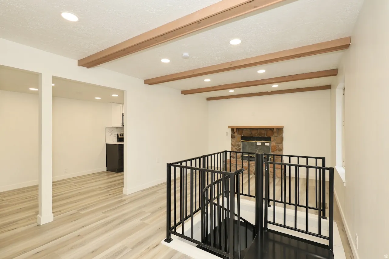 Living area featuring wood-finish flooring, exposed ceiling beams, recessed lighting, and a spiral staircase with black metal railing