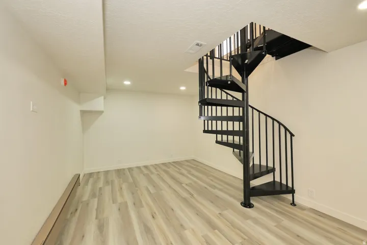 Expansive room featuring a black spiral staircase with metal balusters, wood-finish flooring, recessed lighting, and crisp white walls