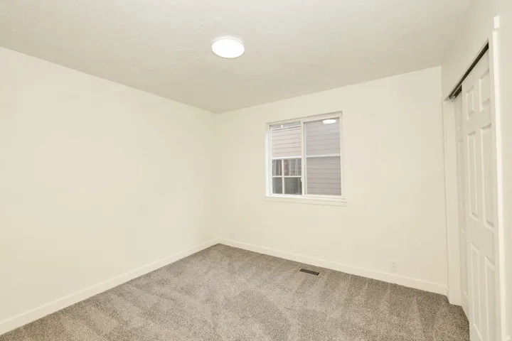 Bright interior space featuring a window with blinds, neutral wall paint, and gray carpet flooring
