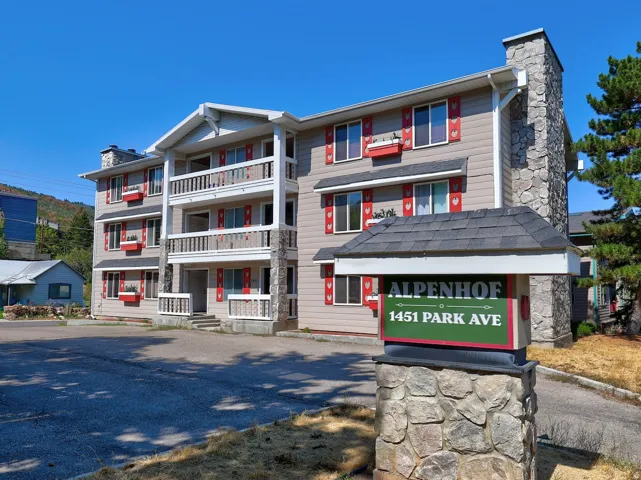 Three-story multi-unit building featuring balconies, red shutters, and stone accents