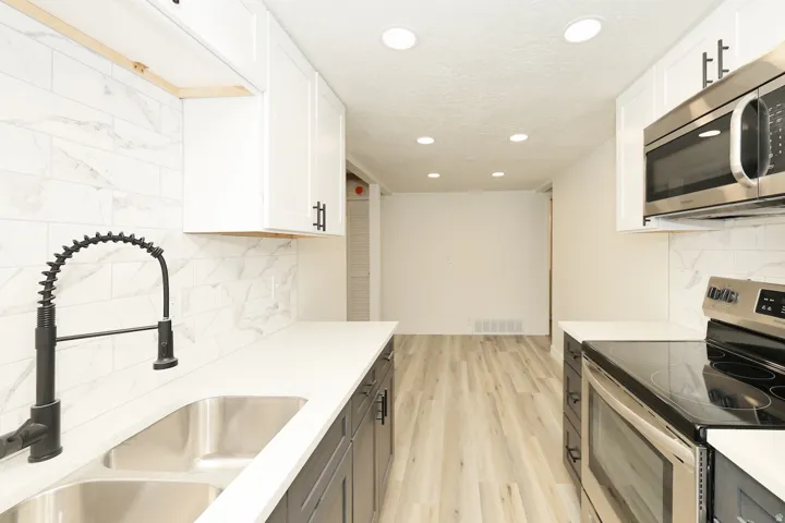 Modern kitchen featuring white upper cabinetry, dark lower cabinetry, light countertops, a double stainless steel sink with a matte black faucet, and a subway tile backsplash