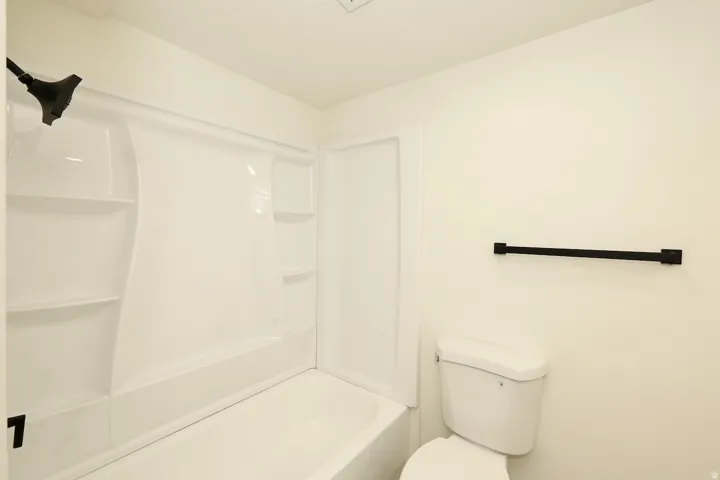White bathtub and shower combination unit featuring an integrated shower head and shelving