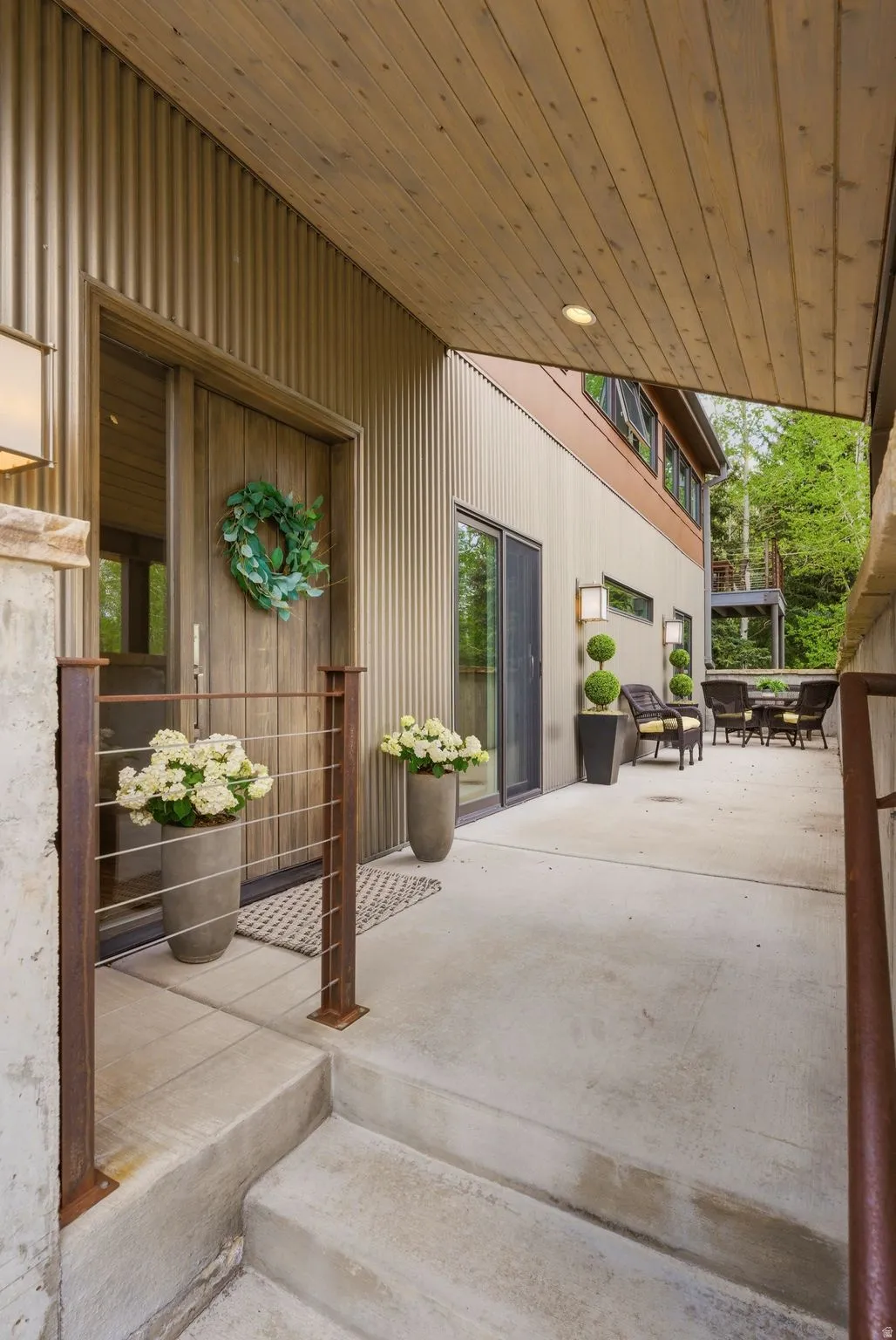 Modern exterior entry featuring a wood-finish door with vertical paneling, corrugated metal siding, and a slatted wood-finish ceiling