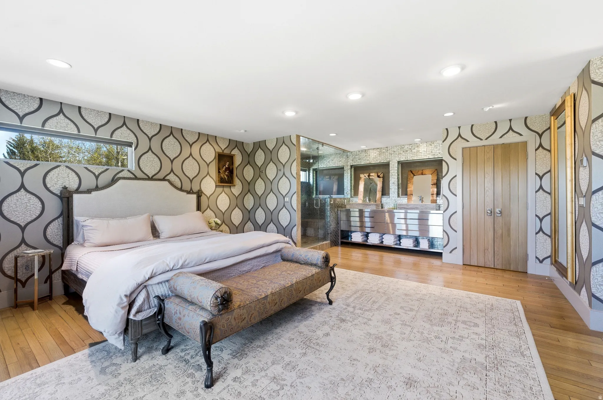 Hardwood flooring extends throughout this expansive room, featuring patterned wall coverings, recessed lighting, and a horizontal window