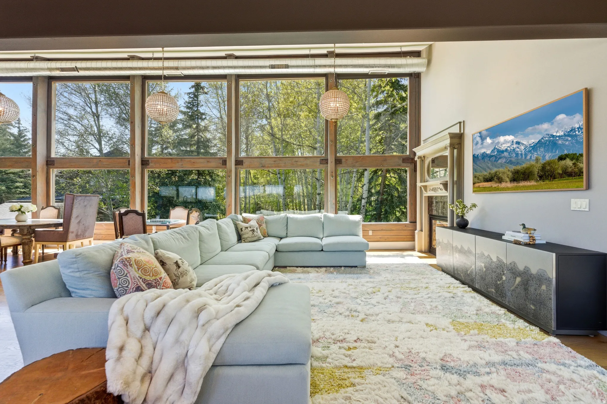 Floor-to-ceiling windows with wood framing, two woven pendant light fixtures, and a decorative fireplace surround with mantel