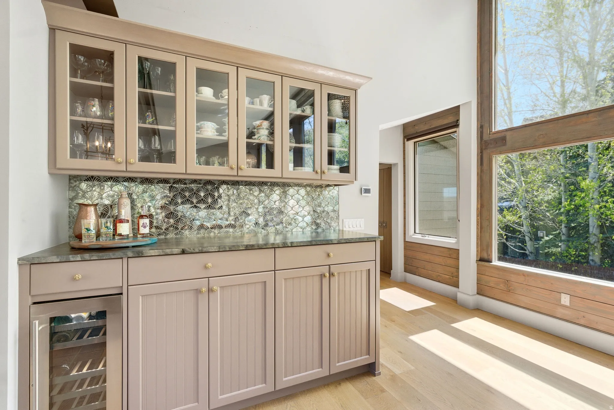 Built-in wet bar featuring upper glass-front cabinetry, a scalloped tile backsplash, stone countertop, and an integrated beverage refrigerator