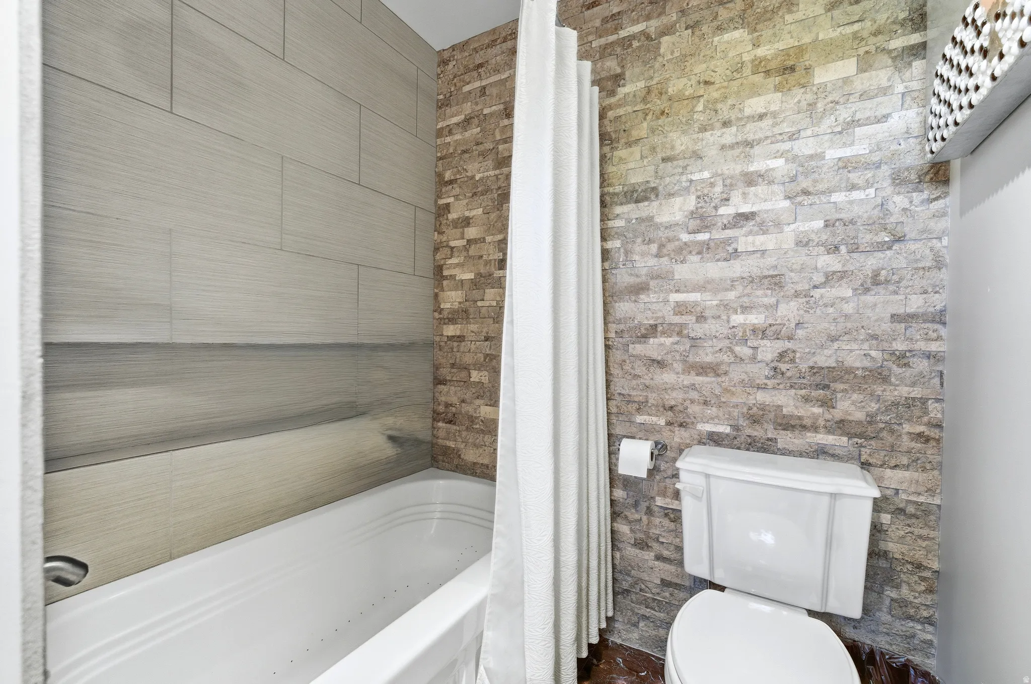 Bathroom featuring a white soaking tub with light gray rectangular wall tiles, complemented by a stacked stone accent wall