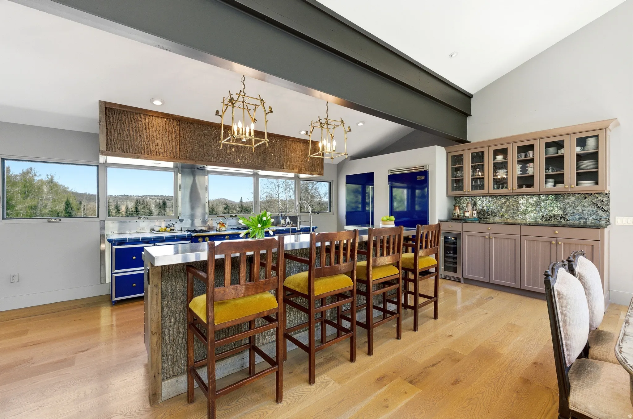 Open-concept kitchen featuring extensive natural light, wood-finish flooring, a wood-clad island with a stainless steel countertop, and a built-in wet bar with glass-front cabinetry