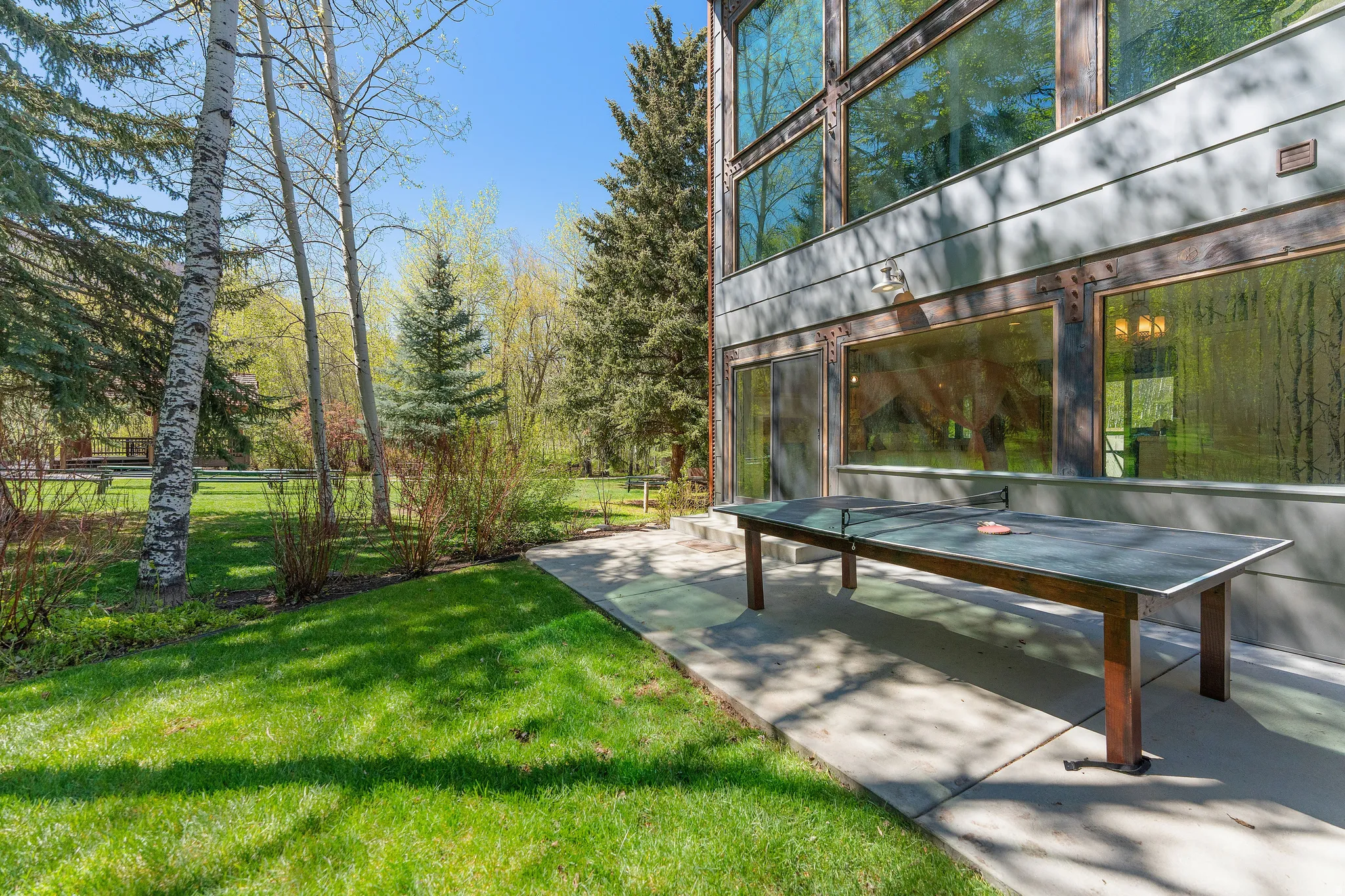 Property exterior featuring expansive multi-pane windows and sliding glass doors, concrete patio, and mature trees