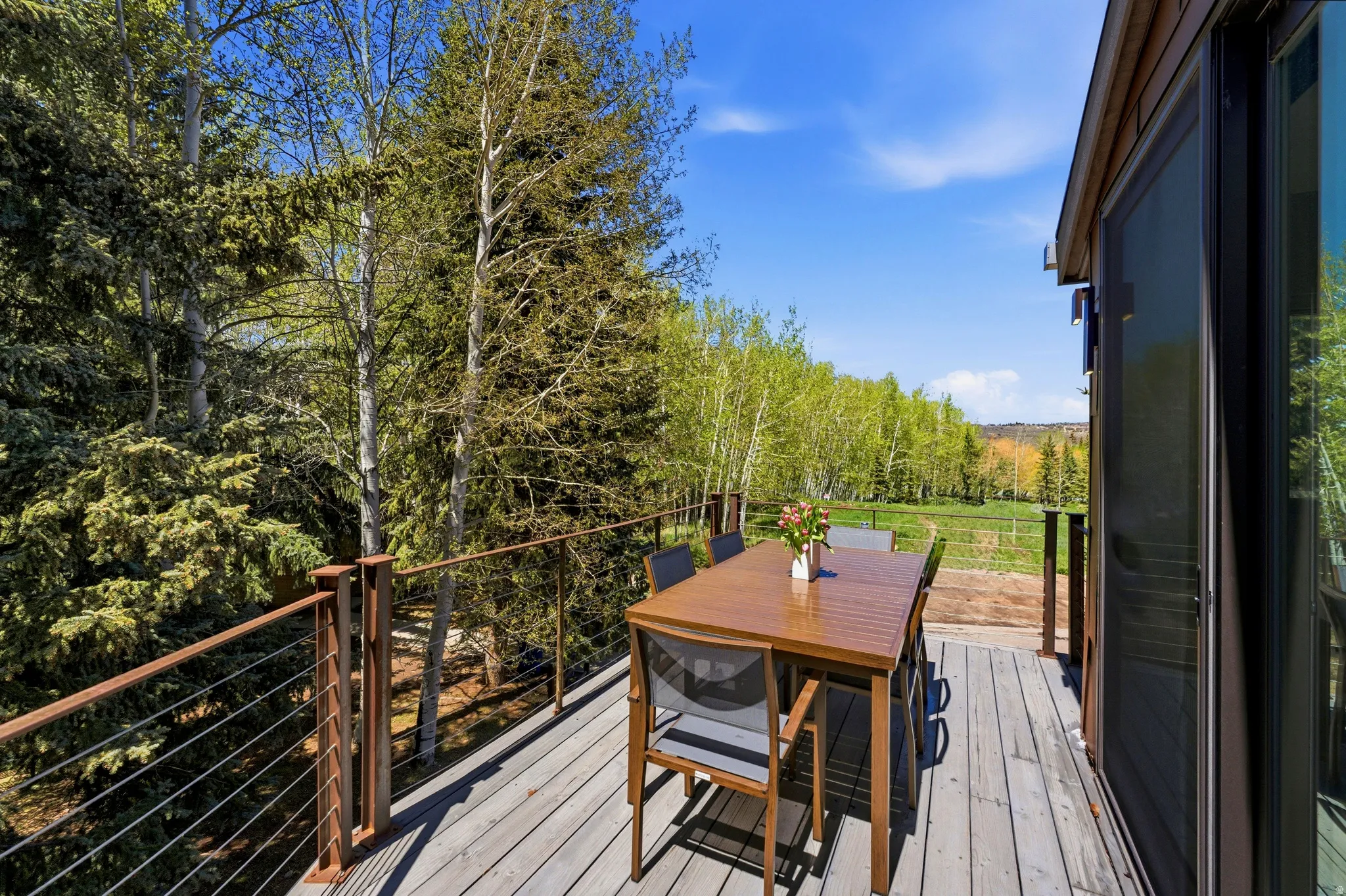 Exterior deck featuring wood-finish flooring, metal railing with horizontal cable infill, and a sliding glass door