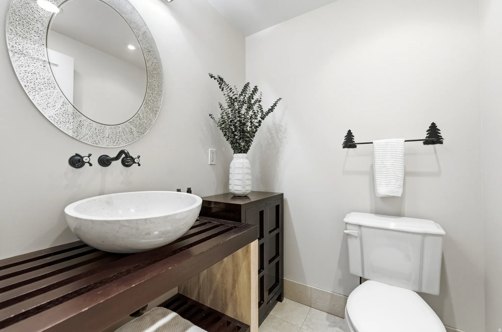Vanity area featuring a stone vessel sink, dark wood-finish countertop, wall-mounted faucet, and a round decorative mirror